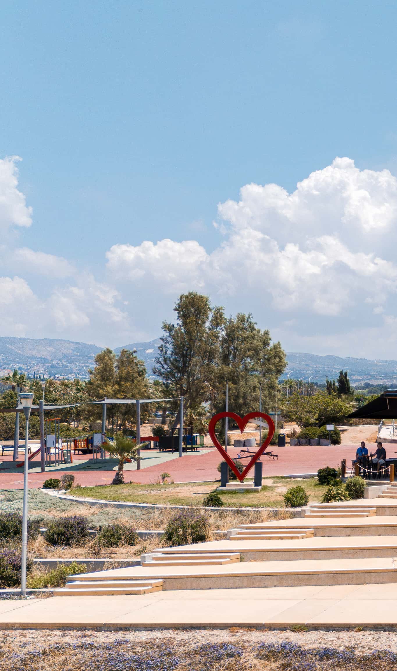 Elevated view over the children's playground and the red heart sculpture, amphitheatre steps in the foreground and hills behind.